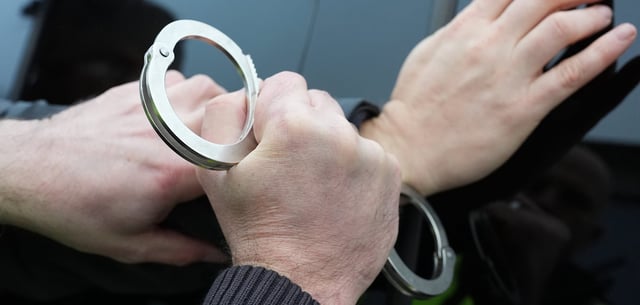 Ein Polizist legt einem Mann Handschellen an 8Symbolfoto)
