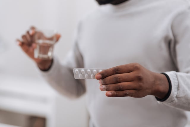 Man holding pill packet with glass of water.