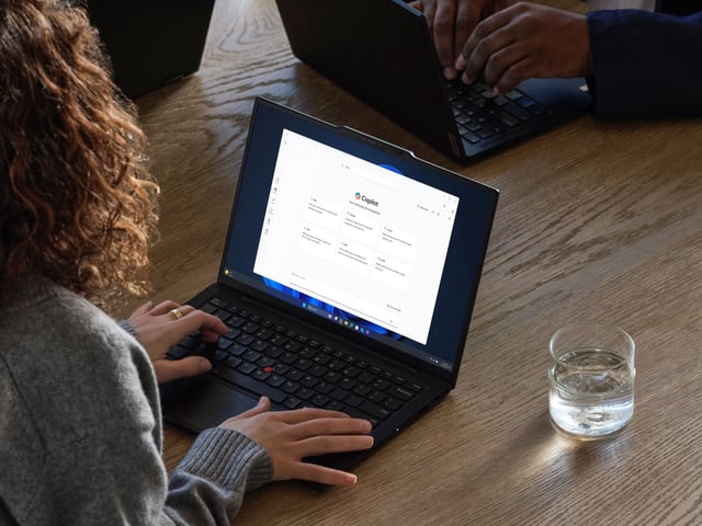 A person at a table with a drinking glass on the right side, working with Copilot.