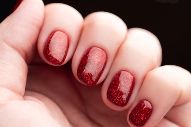 Female hand with beautiful manicure - red glitter gel nails, closeup fingers. Nail care concept