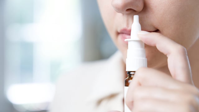 Close-up shot of a young woman using nasal spray