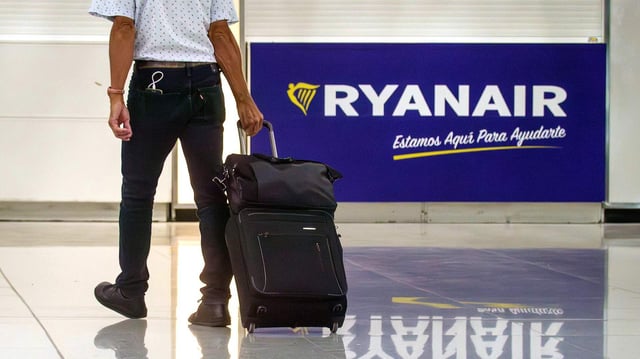 Eine Person mit Handgepäck geht an einem Ryanair-Schild vorbei.