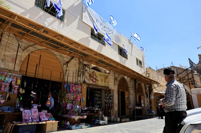 A Palestinian looks at Israeli flags placed over a house which was taken over by Israeli settlers in the old city, in Hebron in the Israeli-occupied West Bank September 3,2025. REUTERS/Mussa Qawasma