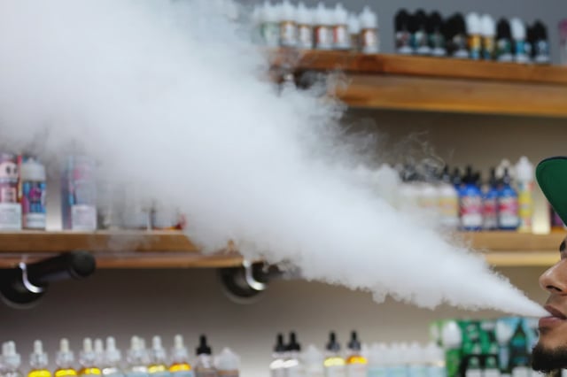 A salesperson at a vape shop in Maine exhales while using an e-cigarette on Sept. 19, 2019.