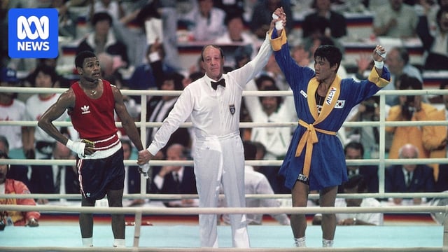 A picture of a boxing referee raising the hand of a South Korean boxer as his American opponent looks stunned.