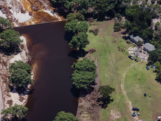 A murky Guadalupe River lurks next to Camp Mystic cabins post July 4th flood. Camper belongings such as blankets and footlockers are spread out across the grass on Tuesday, July 8, 2025.
