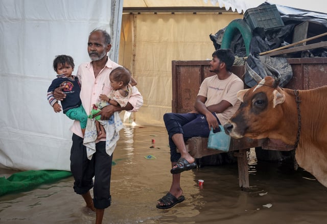 A man wades through a flooded road with his children after a rise in the water level of river Yamuna due to heavy monsoon rains, in New Delhi, India, September 3, 2025. REUTERS/Bhawika Chhabra