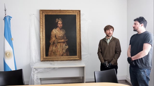 Das Gemälde "Porträt einer Dame" hängt an einer Wand, davor stehen zwei Männer.