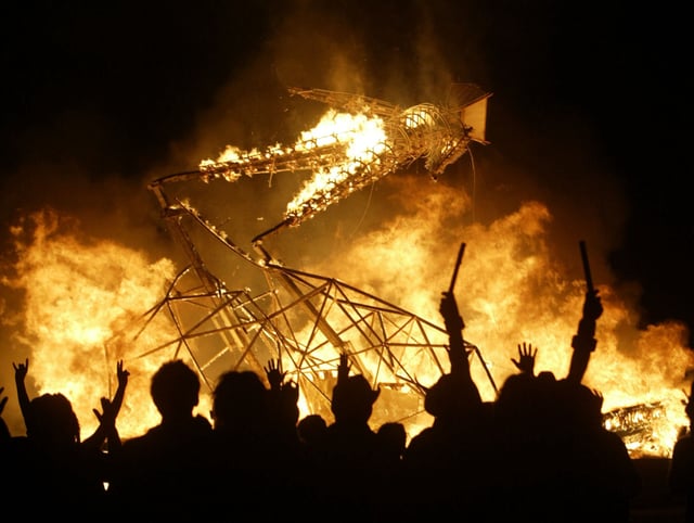 The crowd cheers as the Burning Man topples to the ground at the close of the Burning Man festival Saturday, Sept. 4, 2004, at Black Rock Desert, Nev. (AP Photo/The Chronicle, Lacy Atkins)
