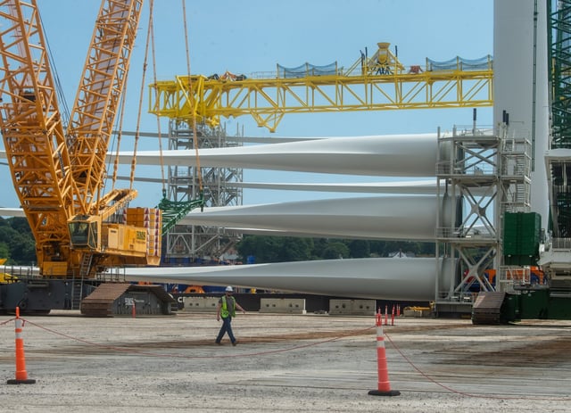 A worker walks past wind turbine blades at the State Pier in New London on Monday, Aug. 25, 2025, ahead of a press conference held in response to the Trump administration’s order to halt construction on the Revolution Wind project. (Aaron Flaum/Hartford Courant)