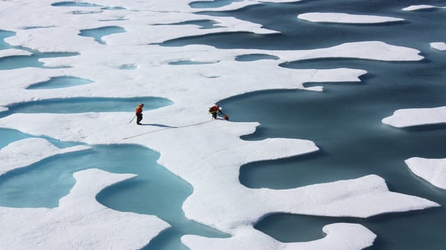 Two scientists walk across melting Arctic sea ice.