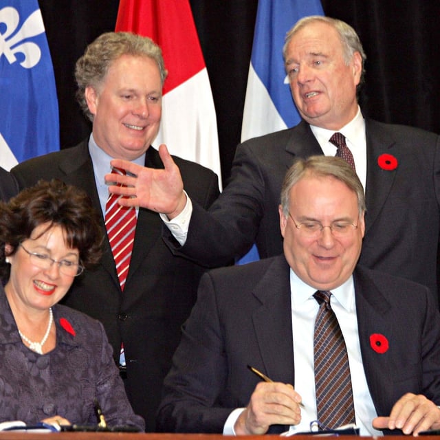 Prime Minister Paul Martin gestures to Quebec Premier Jean Charest as social development Minister Ken Dryden and Carole Theberge sign a child care deal in Montreal, on Friday, Oct. 28, 2005. THE CANADIAN PRESS/Ian Barrett
