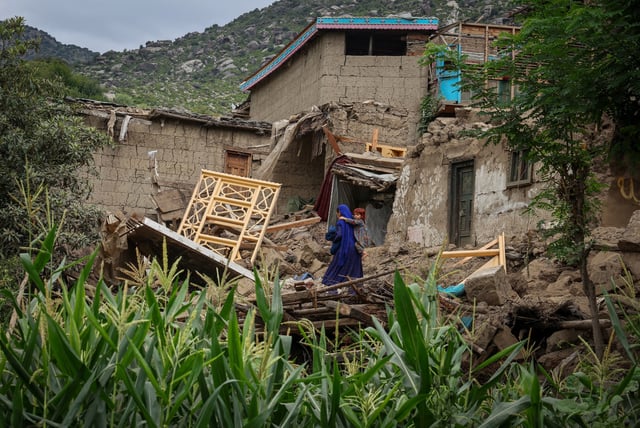 A woman carries a child as she walks past a damaged house following a deadly magnitude-6 earthquake that struck Afghanistan on Sunday, in Mazar Dara, Kunar province, Afghanistan, September 2, 2025. REUTERS/Sayed Hassib