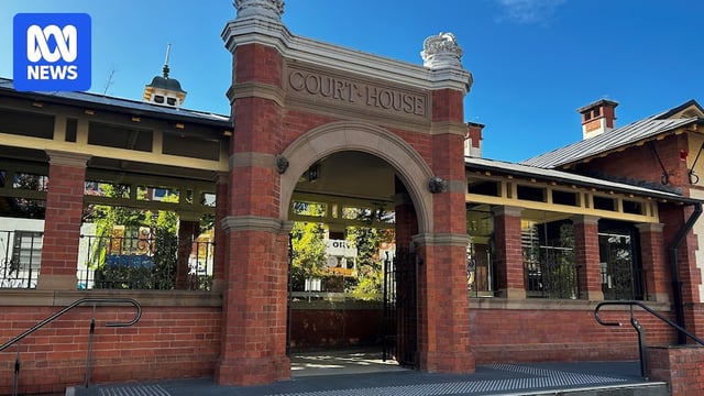 A brick arch in front of a historic-looking building beneath a clear sky.