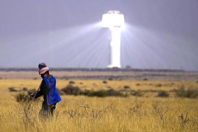 A solar thermal power plant near Upington, South Africa, towers over the landscape while a livestock herder passes by. 