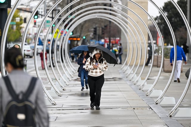 FILE: People with umbrellas walk outside City Hall during a rainy day in San Jose, Calif., March 29, 2023.