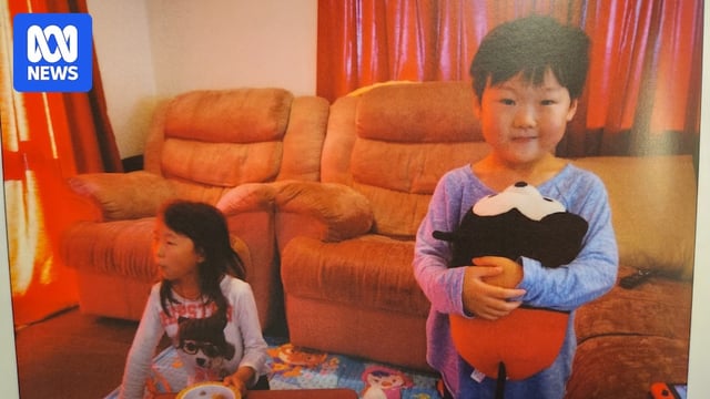 Yuna sits down on the floor while Minu holds a mickey mouse toy.