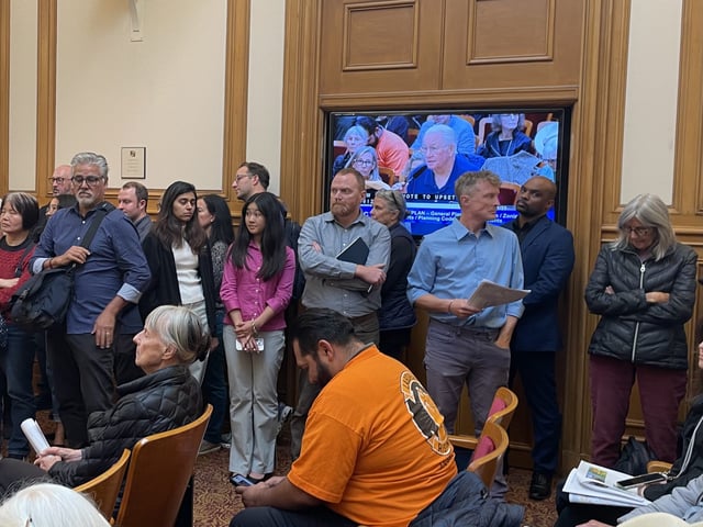 A group of people stand to the side, waiting to give public comment about upzoning at the Planning Commission meeting on September 11, 2025. Photo by Io Yeh Gilman
