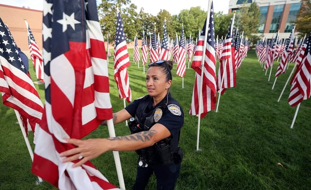 Sandy police officer Adriana Burke unfurls a flag as she and other police officers and firefighters put up flags to honor victims of 9/11 and first responders killed in the line of duty since that day at the Utah Healing Field outside Sandy City Hall in Sandy on Tuesday, Sept. 9, 2025.