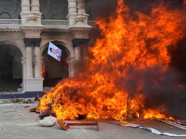 A protester throws a photograph of Nepal Prime Minister Khadga Prasad Oli in the fire at the Singha Durbar, the seat of Nepal's government's various ministries and offices during a protest against social media ban and corruption in Kathmandu, Nepal, Tuesday, Sept. 9, 2025. (AP Photo/Niranjan Shrestha)