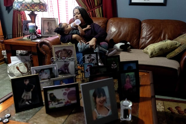 Veronica Kaprosy feeds her granddaughter Italee in the family’s living room. Covering their table are photos of Kaprosy, her husband Daniel and their daughter Danica, who died of fentanyl poisoning in 2022. She was 17 years old.