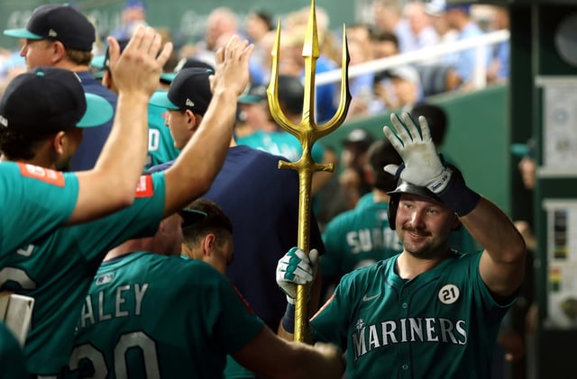 Seattle slugger Cal Raleigh, at right holding trident, is congratulated by teammates in the dugout in the third inning at Kansas City after hitting a 55th home run this season to break Mickey Mantle's record for one-season homers by a switch-hitter