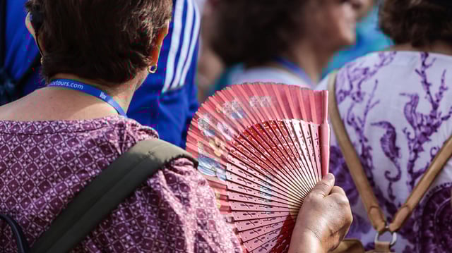 Eine Touristin wedelt sich bei heißem Sommerwetter mit einem Fächer Luft zu.