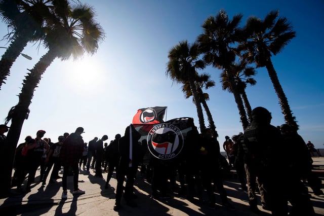 Counter-protesters, some carrying ANTIFA flags, stand beneath palm trees on the beach awaiting to confront demonstrators for a "Patriot March" demonstration in support of US President Donald Trump on January 9, 2021 in the Pacific Beach neighborhood of San Diego, California.