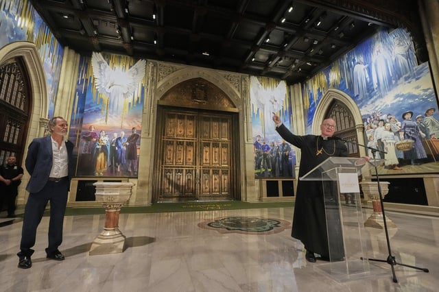 Artist Adam Cvijanovic, left, listens as Cardinal Timothy Dolan speaks during a media preview of the 25-foot-high mural, the largest artwork ever commissioned for St. Patrick's Cathedral, in New York, Thursday, Sept. 18, 2025. (AP Photo/Richard Drew)