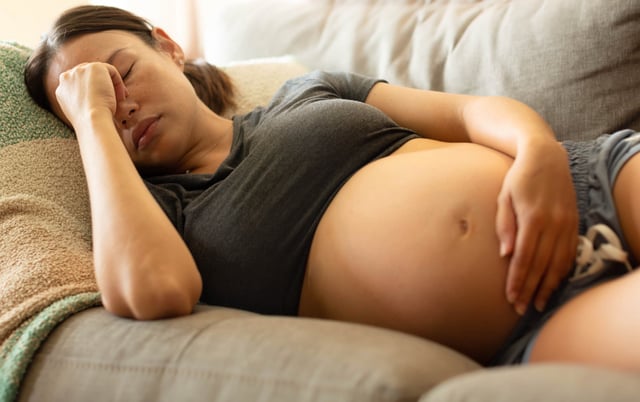 An uncomfortable pregnant mother trying to rest at home, lying on her couch holding her head.