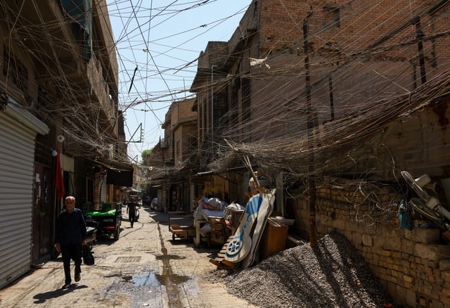 People walk along an old street as a tangled web of electrical wires from a generator supplying homes with electricity hangs above buildings, in Baghdad, Iraq, September 10, 2025. REUTERS/Thaier Al-Sudani