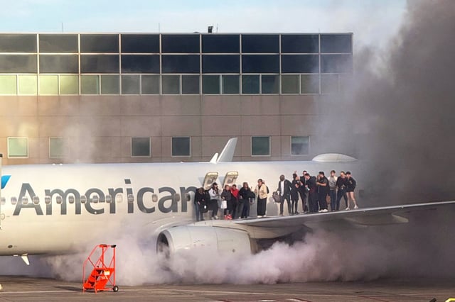 Passengers stand on the wing of an American Airlines plane as they are evacuated after it caught fire while at a gate at Denver International Airport in Denver, on March 13, 2025.