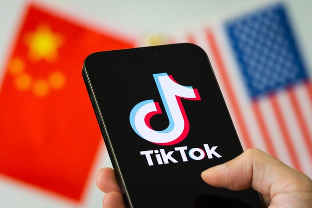 In this photo illustration, a smartphone displays the logo of TikTok, the short-video social media platform owned by China’s ByteDance Ltd., with the national flags of China and the United States shown in the background on September 16, 2025 in Chongqing, China.