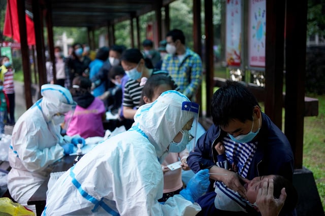 A medical worker in a protective suit conducts a nucleic acid testing for a child at a residential compound in Wuhan, the Chinese city hit hardest by the coronavirus disease (COVID-19) outbreak, Hubei province, China May 14, 2020. REUTERS/Aly Song/File Photo
