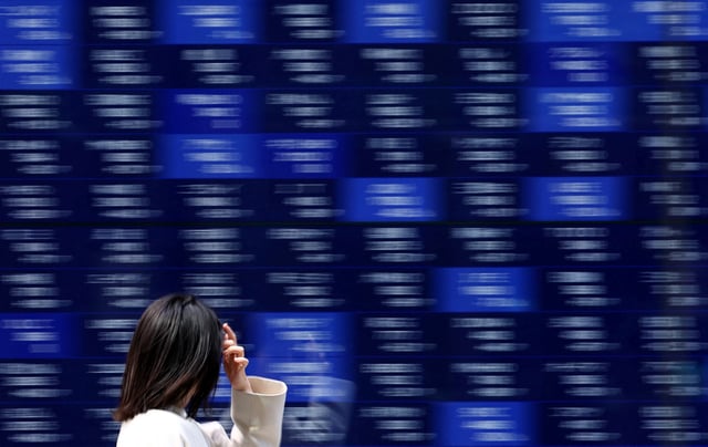 A woman walks past an electronic screen displaying stock quotation board in Tokyo, Japan April 15, 2025. REUTERS/Issei Kato/File Photo