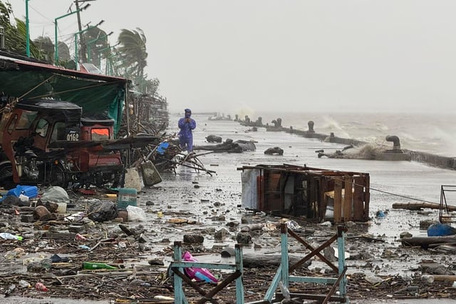 A man stands near debris on a waterfront road amid heavy rain due to weather patterns from Super Typhoon Ragasa in Aparri town, Cagayan province on September 22, 2025.