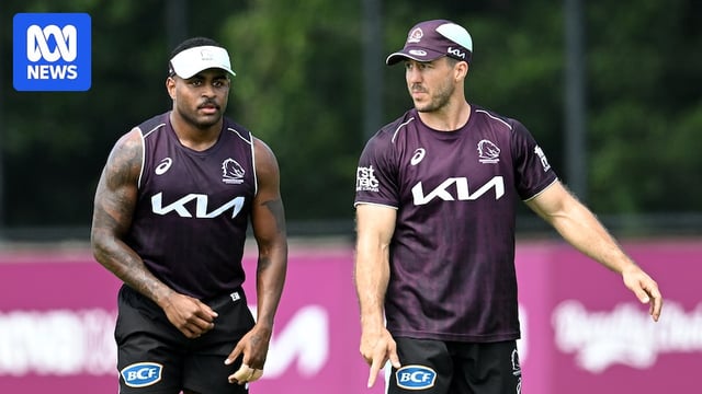 Two Brisbane Broncos players stand next to each other at training as the one on the right looks at his partner.
