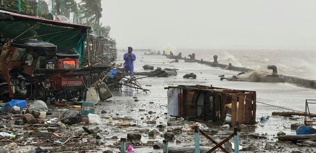 Un homme se tient à côté de débris près du bord de mer, le 22 septembre 2025 à Aparri aux Philippines