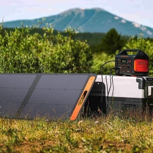 the jackery explorer 500 portable power station in a camping setting with a solar panel charging it