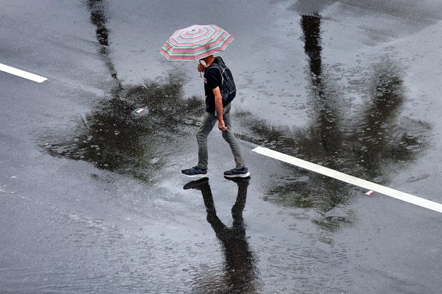 A man takes cover from the rain under his umbrella as he crosses the street at Young Circle in Hollywood on Wednesday, July 23, 2025.  The forecast calls for more showers and thunderstorms - some locally heavy downpours are possible today and tomorrow.   (Mike Stocker/South Florida Sun Sentinel)