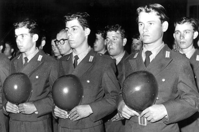 schwarz-weiss Foto - junge Männer in Uniform halten den Helm in der Hand und schauen ernst