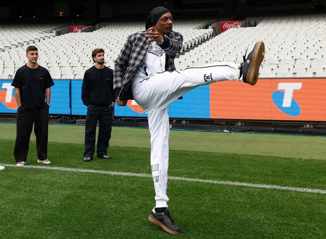 Snoop Dogg kicks a goal as Nick Daicos and Josh Daicos of the Magpies look on during an AFL Telstra Grand Final Entertainment Media Opportunity.