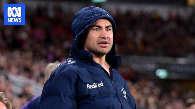 A Melbourne Storm player stands on the sidelines wearing a jacket with a hood on.