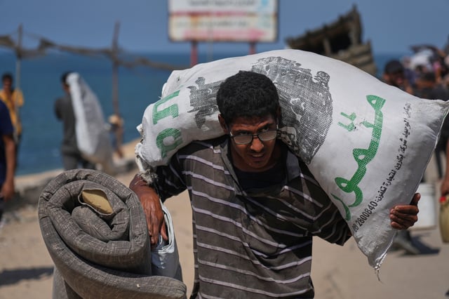 A displaced Palestinian flees northern Gaza Strip, carrying his belongings along the coastal road, near Wadi Gaza, Tuesday, Sept. 23, 2025. (AP Photo/Abdel Kareem Hana)