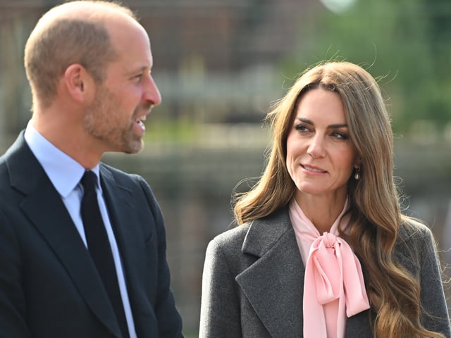 Kate Middleton wearing a gray suit and pink blouse smiling