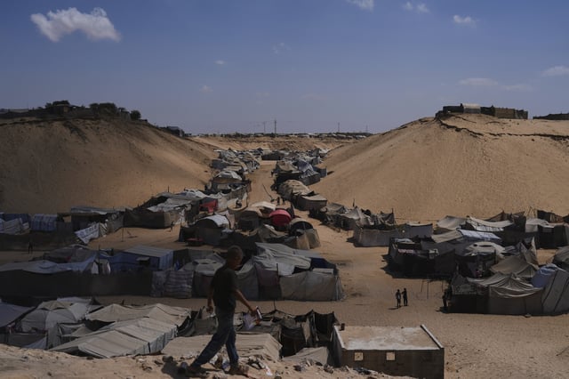 Displaced Palestinians walks through a tent camp in Muwasi, an area that Israel has designated as a safe zone, in Khan Younis southern Gaza Strip, Sunday, Sept. 21, 2025. (AP Photo/Jehad Alshrafi)