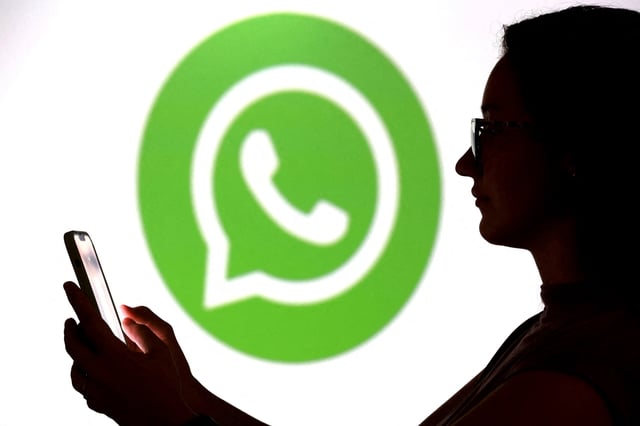 A teenager poses for a photo while holding a smartphone in front of a Whatsapp logo in this illustration taken September 11, 2025. REUTERS/Dado Ruvic/Illustration/File Photo