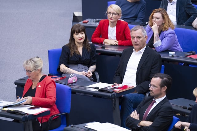 Heidi Reichinnek mit rosa Handtäschchen, Jan van Aken ohne Schlips und Ines Schwerdtner in rotem Jackett (hinten) sitzen im Bundestag