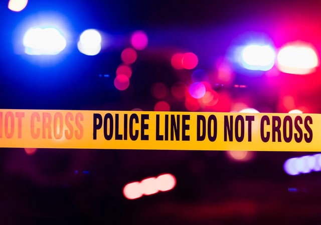 Emergency lights of police cars flashing blue, red and white in the background.