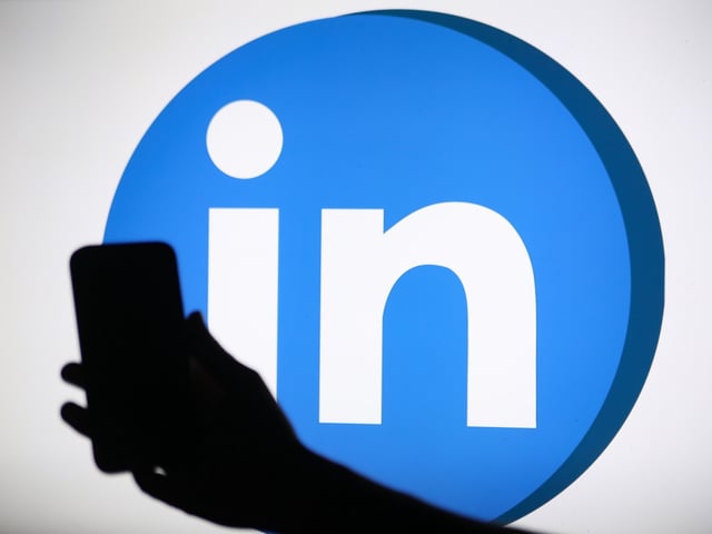 The LinkedIn logo displays on a screen with a person holding a phone
